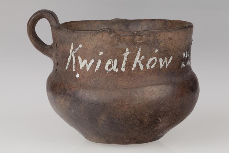 kubek z taśmowatym uchem, obok ucha pionowe rzędy otworków  