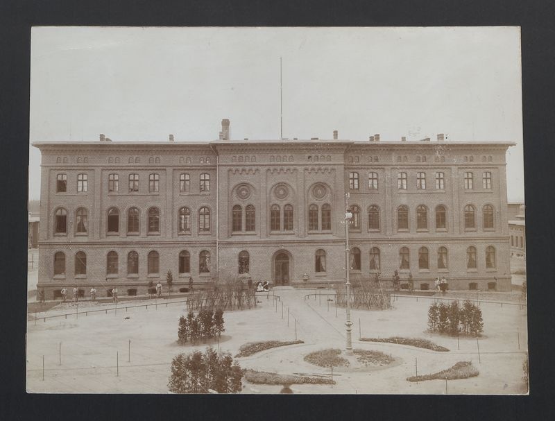 Gniezno – Dziekanka. Budynek administracyjny, na jego tle pracownicy opiekujący się zielenią.