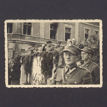 Uroczystości 3-go Maja w Gnieźnie. Uczestnicy pochodu na tle trybuny ustawionej przed budynkiem, na narożniku ulic Chrobrego i Mieszka I 